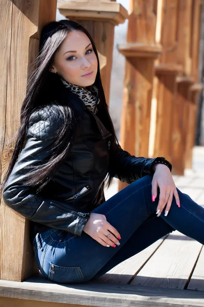 Young brunette woman sitting leaning against a wooden post — Stock Photo, Image