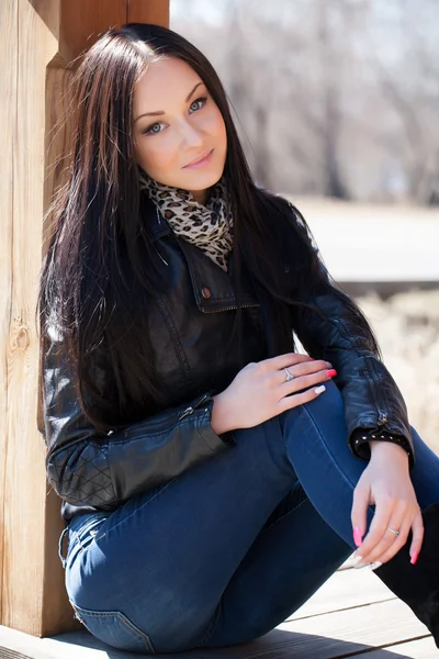 Young brunette woman sitting leaning against a wooden post — Stock Photo, Image