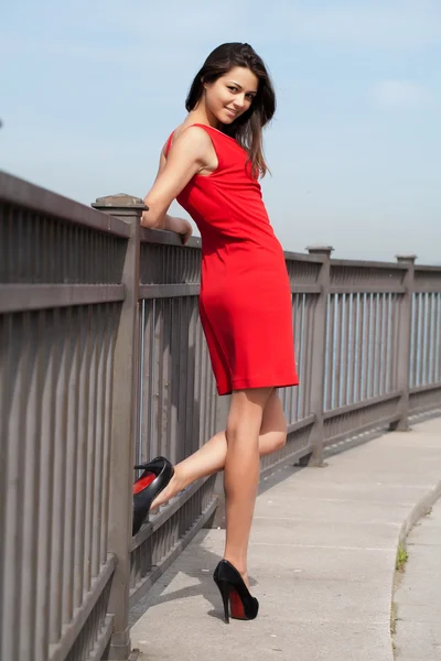 Girl in the red dress standing at the metal fence — Stock Photo, Image