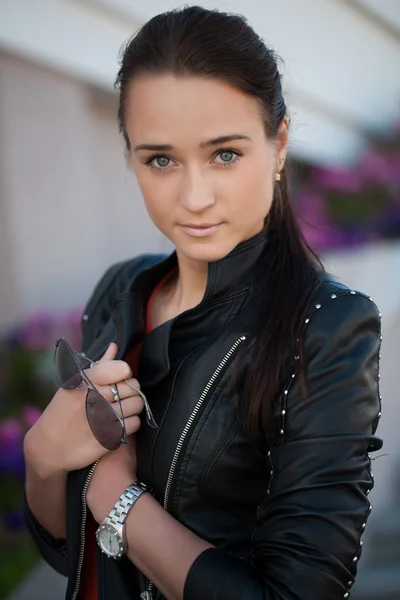 Girl in leather jacket with sunglasses in hand — Stock Photo, Image