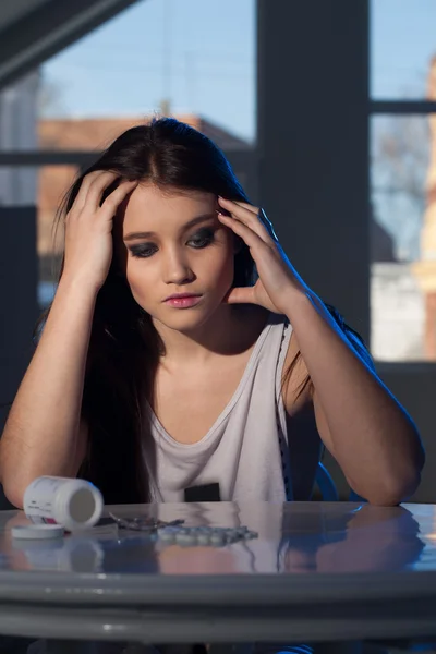Молодая девушка сидит за столом с рассеянными таблетками — стоковое фото