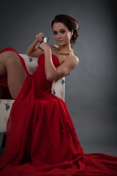 美丽的女孩穿着红色晚礼服坐在椅子上 — 图库照片