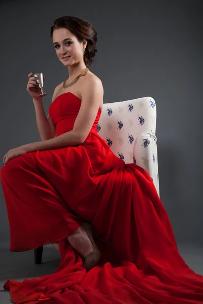 Beautiful girl in red evening dress sitting in a chair — Stock Photo, Image