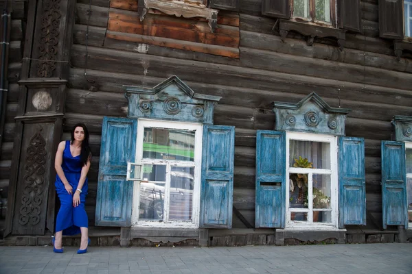 Meisje in een blauwe jurk op een achtergrond van een oud houten huis — Stockfoto