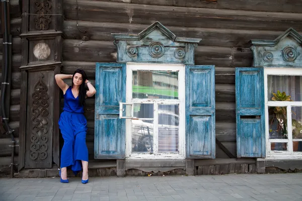 Meisje in een blauwe jurk op een achtergrond van een oud houten huis — Stockfoto