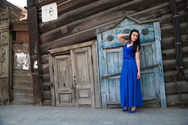 Girl in a blue dress on a background of an old wooden house — Stock Photo, Image