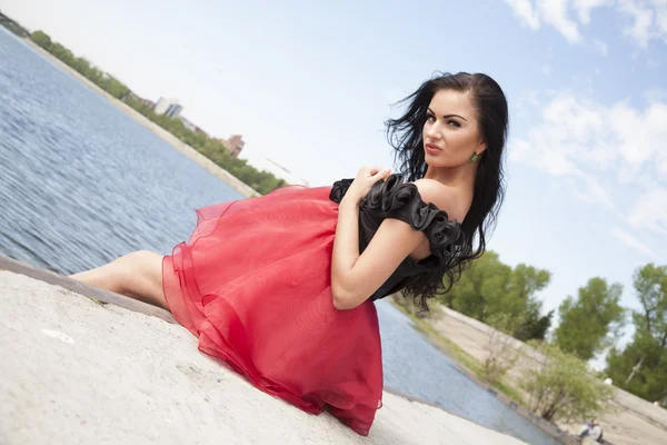 Dívka v červených šatech na břehu řeky — Stock fotografie