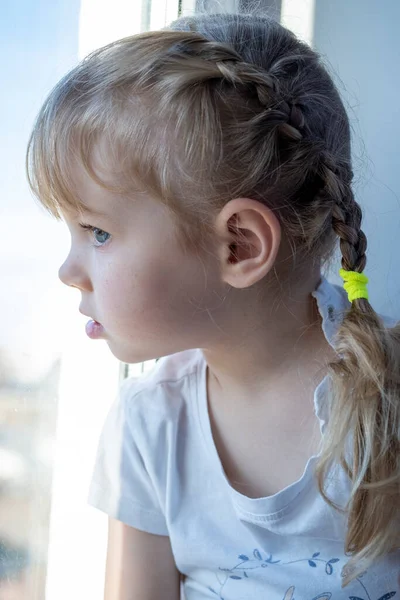 小さな女の子は窓の上に座って窓の外を見る — ストック写真