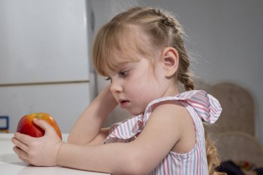 Büyük kırmızı elmalı küçük kız odadaki masada oturuyor.