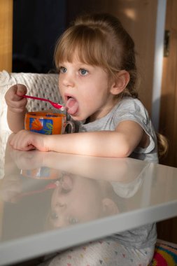 Kız masaya oturur ve bir kupadan dondurma yer.