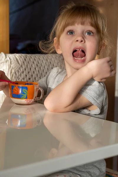 女の子はテーブルに座ってマグカップからアイスクリームを食べる — ストック写真