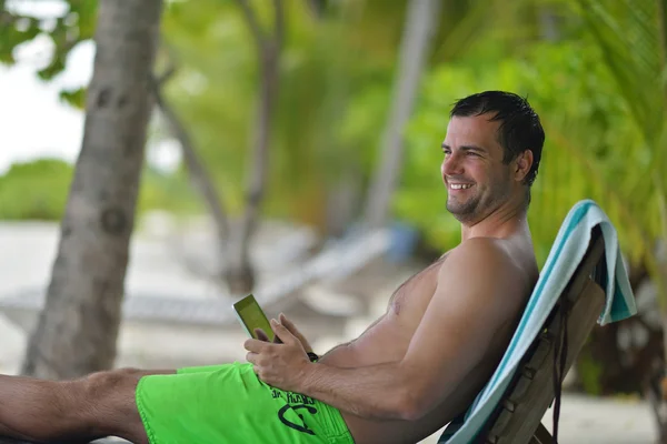 Homem ralaxing e utilizar comprimido na praia — Fotografia de Stock