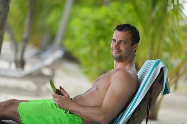 Hombre ralaxing y el uso de tabletas en la playa —  Fotos de Stock