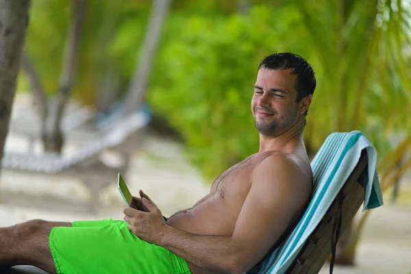 Человек ralaxing и использовать планшет на пляже — стоковое фото