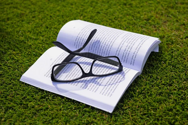 Γυαλιά σε ένα βιβλίο εκτός με χόρτο — Φωτογραφία Αρχείου