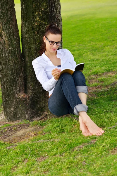 Νεαρή γυναίκα διαβάζει ένα βιβλίο στο πάρκο — Φωτογραφία Αρχείου