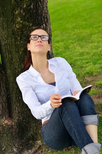 Ung kvinna läser en bok i parken — Stockfoto