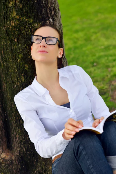 Ung kvinna läser en bok i parken — Stockfoto