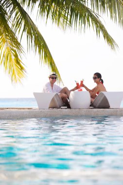 Genç çift rahatla ve taze içecekler havuz kenarında al