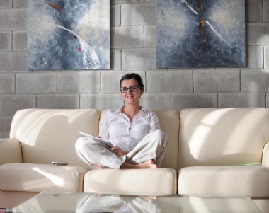 Evde tablet bilgisayar kullanan genç bir kadın.