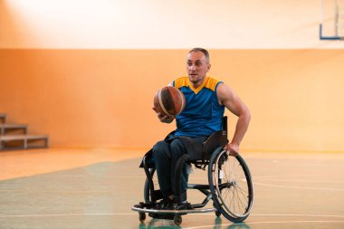 Tekerlekli sandalye ve engelli savaş gazilerinin sahada basketbol oynarken çekilmiş yakın bir fotoğrafı.