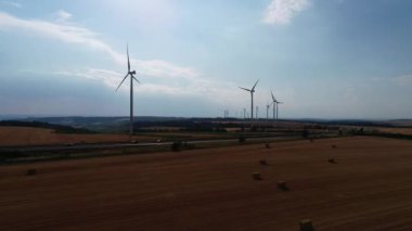 Geniş rüzgar türbinleri. Saha manzaralı, parlak turuncu günbatımı. Mavi gökyüzü parkı yavaş çekim drone dönüşü. Siluetler yel değirmenleri, büyük turuncu güneş diski yaz merceği parlamaları. Alternatif enerji