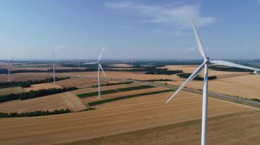 Geniş rüzgar türbinleri. Saha manzaralı, parlak turuncu günbatımı. Mavi gökyüzü parkı yavaş çekim drone dönüşü. Siluetler yel değirmenleri, büyük turuncu güneş diski yaz merceği parlamaları. Alternatif enerji