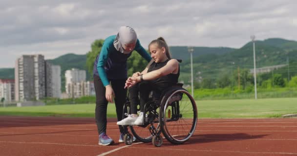 Grupa wielokulturowych sportowców niepełnosprawna kobieta i jej trener noszący hidżab po treningu na lekkoatletyce tor sportowy sprawdzanie danych na smartwatch. — Wideo stockowe