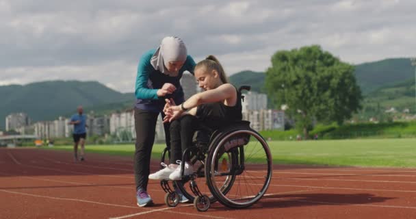 Ryhmä monikulttuurisen urheilun ihmiset vammainen nainen ja hänen kouluttaja yllään hijabia harjoittelun jälkeen yleisurheilun urheiluradalla tarkistaa tietoja älykello. — kuvapankkivideo