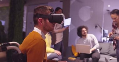 Modern açık uzay ofisinde çalışan engelli bir iş adamı sanal gerçeklik gözlüğü ve İHA simülasyonu kullanarak takım toplantısı yapıyor. Girişim işinde etkin takım çalışması.