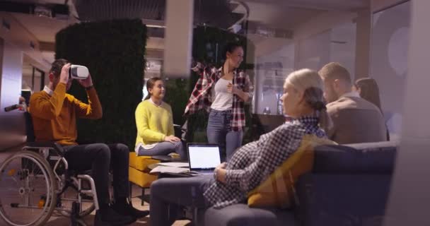 Niepełnosprawny biznesmen na wózku inwalidzkim w pracy w nowoczesnym biurze współpracowników na otwartej przestrzeni na spotkaniu zespołowym z wykorzystaniem gogli wirtualnej rzeczywistości i symulacji dronów. Skuteczna praca zespołowa w biznesie startującym. — Wideo stockowe