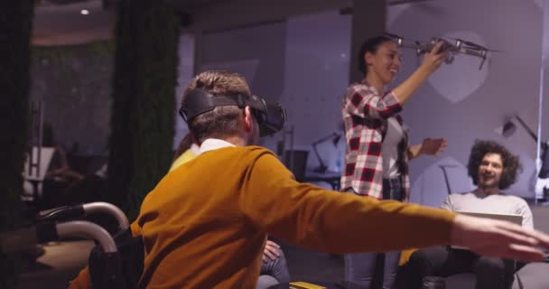 Empresário com deficiência em uma cadeira de rodas no trabalho em um moderno escritório de coworking de espaço aberto em reunião de equipe usando óculos de realidade virtual e simulação de drones. Trabalho em equipe eficaz em um negócio de startup. — Vídeo de Stock