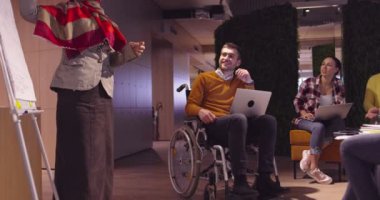 Modern bir açık alanda çalışan Müslüman bir kadın takıma bir sunum yapıyor. Orta Doğulu Arap iş kadını yaratıcı bir ofiste. Ekip toplantısında tekerlekli sandalyedeki engelli iş adamı 