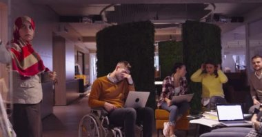 Modern bir açık alanda çalışan Müslüman bir kadın takıma bir sunum yapıyor. Orta Doğulu Arap iş kadını yaratıcı bir ofiste. Ekip toplantısında tekerlekli sandalyedeki engelli iş adamı 
