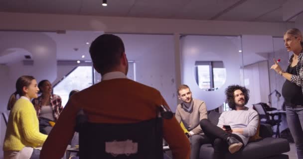 장애인 사업가가 휠체어를 타고 현대의 오픈 우주 직장에서 팀 미팅에서 일하고 있습니다. 스타트업 사업에 효과적 인 팀워크와 포함. — 비디오