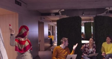Modern bir açık alanda çalışan Müslüman bir kadın takıma bir sunum yapıyor. Orta Doğulu Arap iş kadını yaratıcı bir ofiste. Ekip toplantısında tekerlekli sandalyedeki engelli iş adamı 