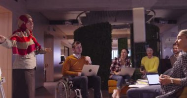 Modern bir açık alanda çalışan Müslüman bir kadın takıma bir sunum yapıyor. Orta Doğulu Arap iş kadını yaratıcı bir ofiste. Ekip toplantısında tekerlekli sandalyedeki engelli iş adamı 