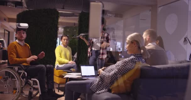 Gehandicapte zakenman in een rolstoel aan het werk in moderne open ruimte coworking office op teamvergadering met behulp van virtual reality bril en drone simulatie. Effectief teamwerk in een startup business. — Stockvideo