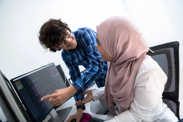 Start-up-Unternehmen, junge Kreative diskutieren über Treffen im hellen Büro, während sie auf einen Dual-Monitor-Computer für Vorschläge und Hilfe im Projekt zeigen — Stockfoto