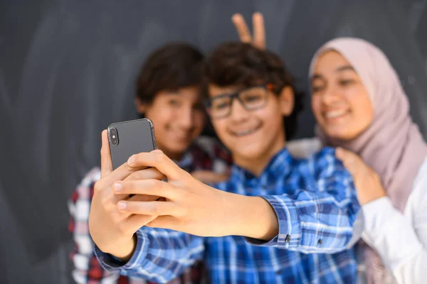 Gruppo di adolescenti arabi che scattano foto di selfie su smartphone con lavagna nera in background. Focus selettivo — Foto Stock