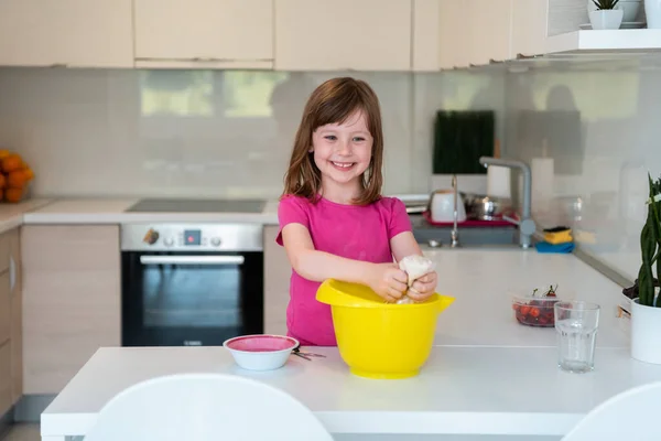 Маленькая девочка готовит тесто в подводном смесителе и облизывает его пальцы. Современная бытовая техника удобна и проста даже для детей. хобби кулинарии. Селективный фокус — стоковое фото