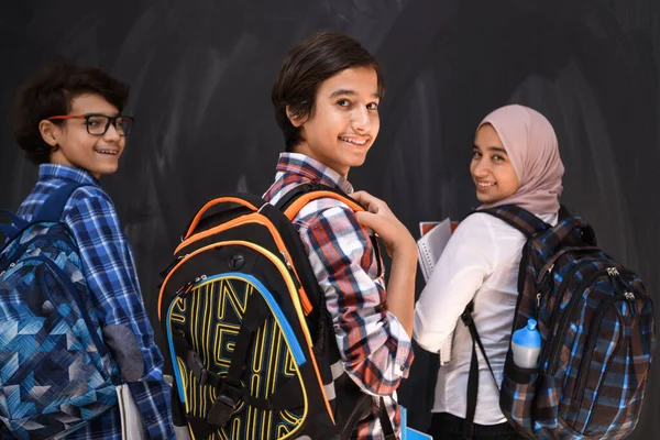 Adolescenti arabi, studenti ritratto di gruppo contro lavagna nera indossando zaino e libri a scuola.Focus selettivo — Foto Stock