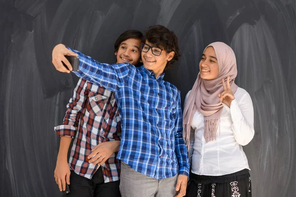 Gruppe arabischer Teenager macht Selfie-Foto mit Smartphone und schwarzer Kreidetafel im Hintergrund. Selektiver Fokus — Stockfoto