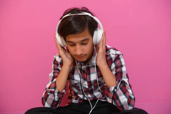 Arabisch tiener jongen dragen hoofdtelefoon en luisteren naar muziek roze achtergrond — Stockfoto