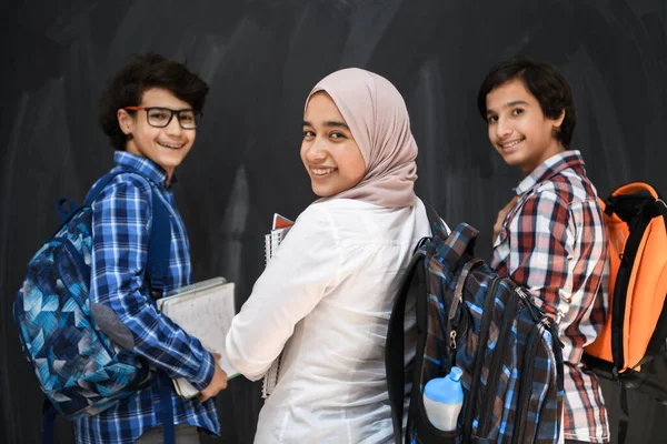 在学校里，阿拉伯青少年，学生们穿着背包和书本，把肖像与黑色黑板相对照。有选择的焦点 — 图库照片