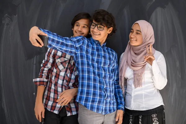Gruppe arabischer Teenager macht Selfie-Foto mit Smartphone und schwarzer Kreidetafel im Hintergrund. Selektiver Fokus — Stockfoto