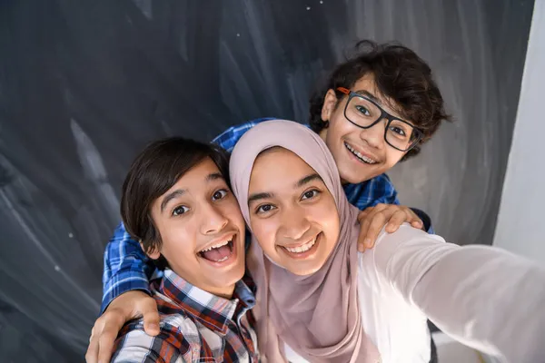 Gruppo di adolescenti arabi che scattano foto di selfie su smartphone con lavagna nera in background. Focus selettivo — Foto Stock