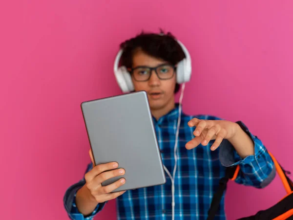 Portret van een arabische tiener met hoofdtelefoon, een rugzak en een tablet geïsoleerd op een paarse achtergrond tijdens het kijken naar online lessen tijdens de corona virus pandemie — Stockfoto