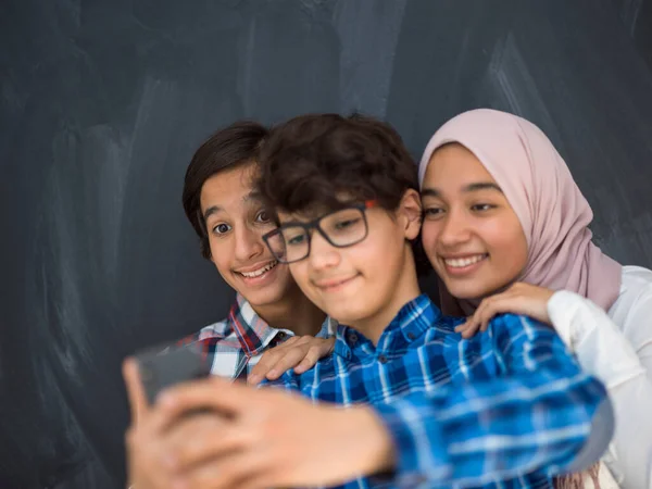 Groep van arabische tieners het nemen van selfie foto op smartphone met zwart krijtbord op de achtergrond — Stockfoto