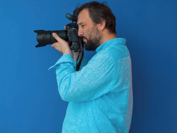 Retrato del fotógrafo masculino en camisa azul sosteniendo la vieja cámara de arte analógica slr mientras está de pie sobre el fondo cian — Foto de Stock